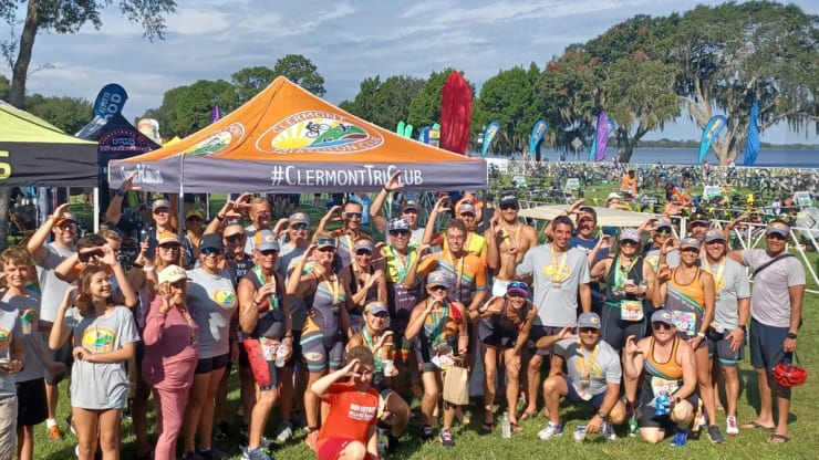 Members of the Clermont Tri Club pose for a photo at a race. Many are forming the letter C with their hand.